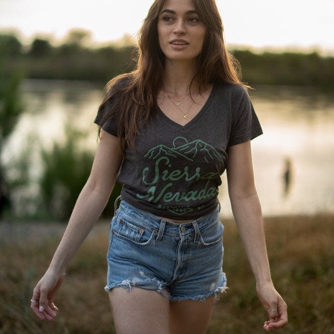 A woman wears the Sierra Nevada Brewing Co. 1980 v-neck t-shirt as she walks away from the edge of a river.