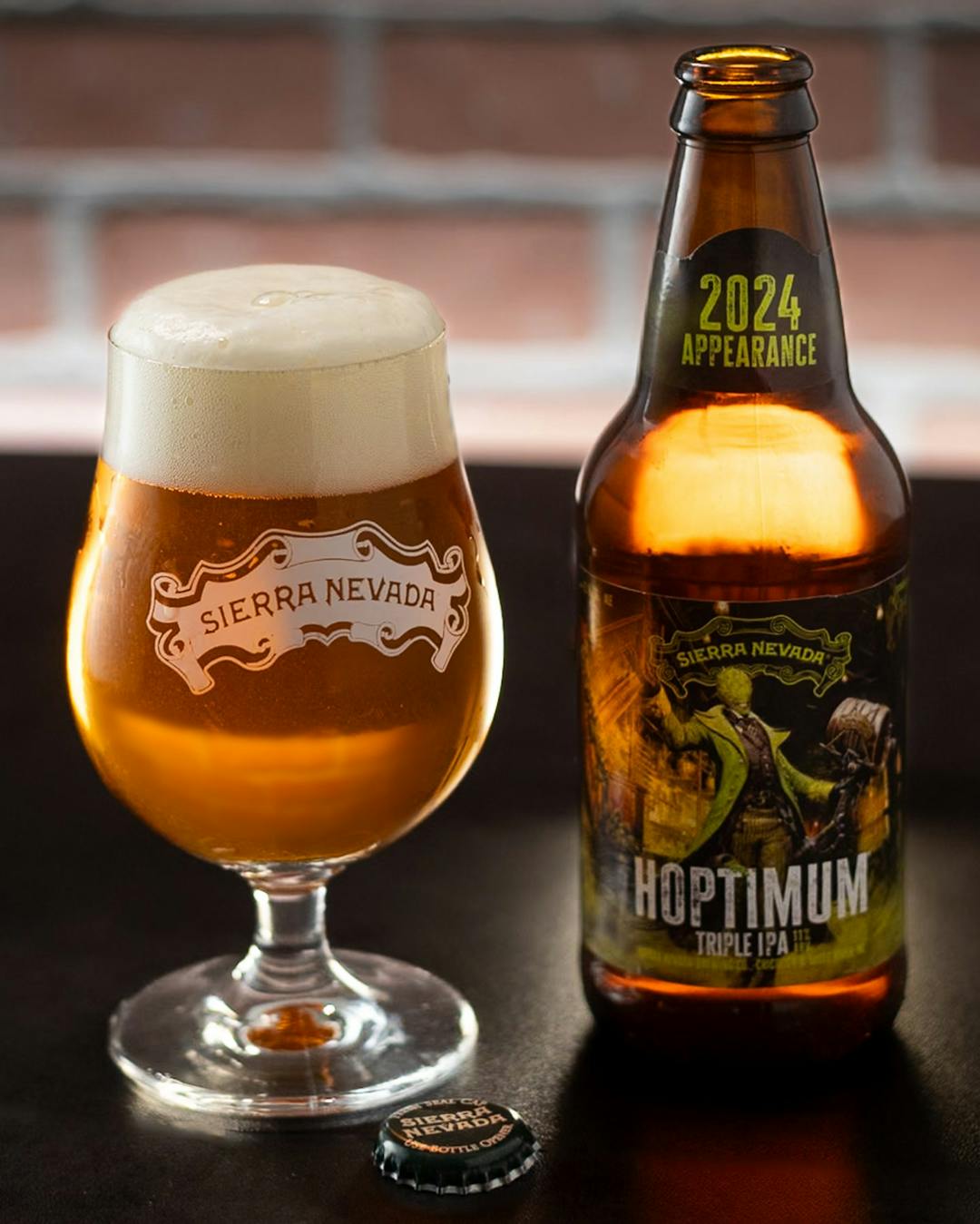 A full glass and a bottle of Hoptimum Triple IPA on a dark table with a bottle cap in the foreground