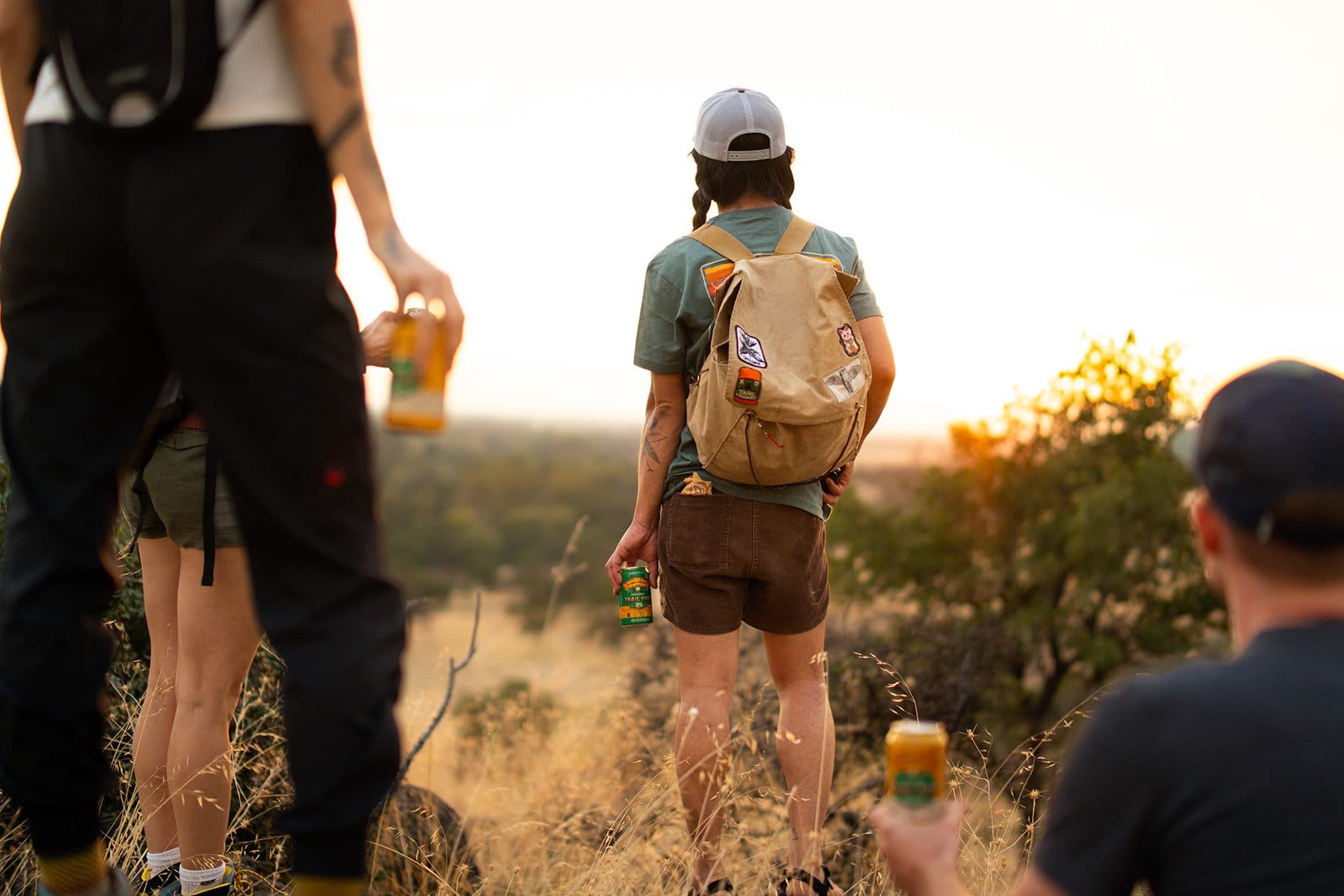 Four friends watching a sunset and holding cans of non-alcoholic Sierra Nevada Trail Pass