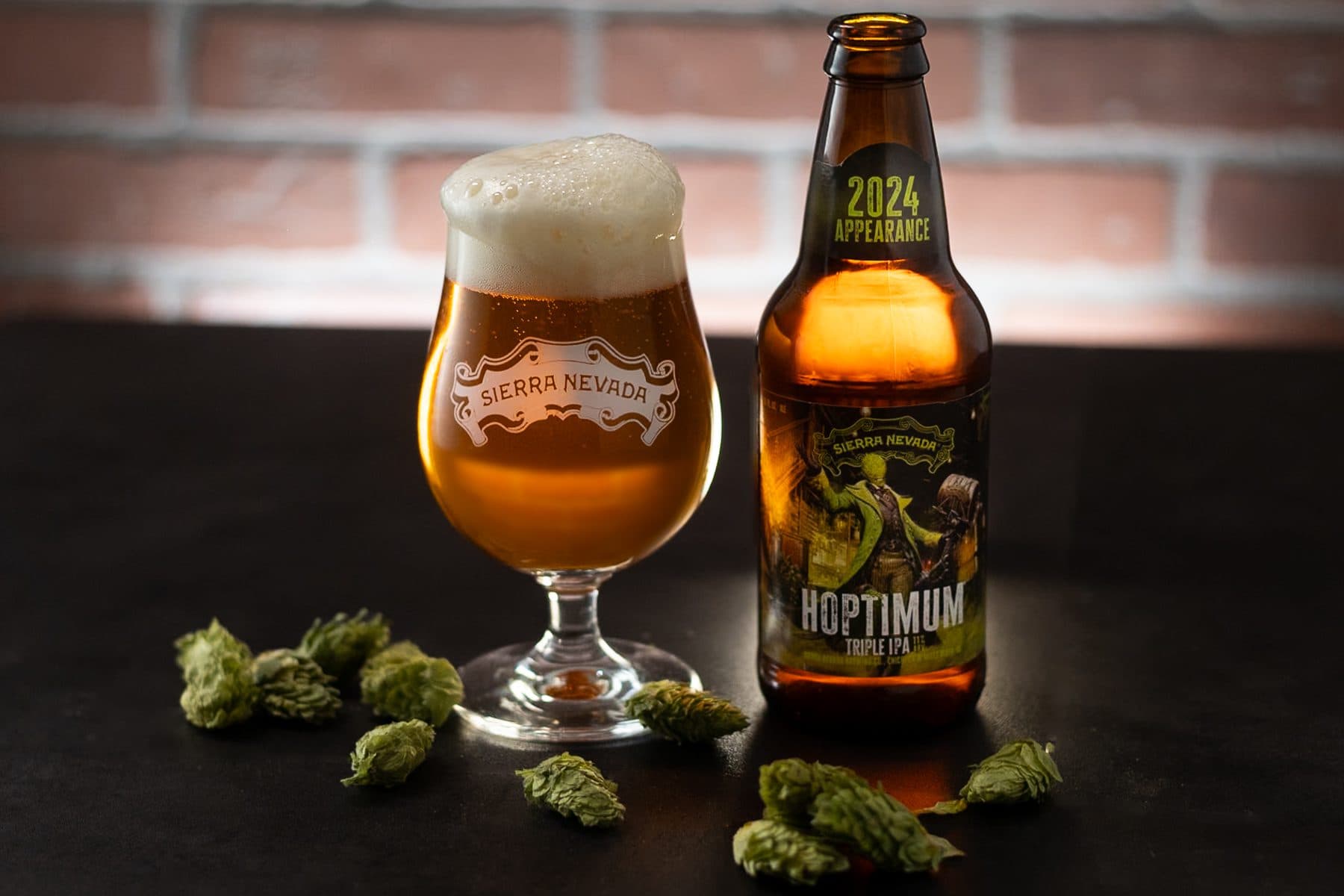 A full glass and a bottle of Hoptimum Triple IPA on a dark table with several hop cones in the foreground