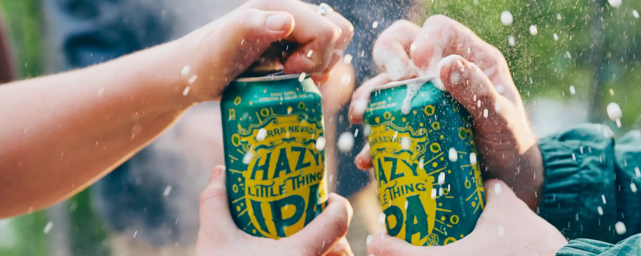 Hands opening cans of Hazy Little Thing with foam spraying out of the top