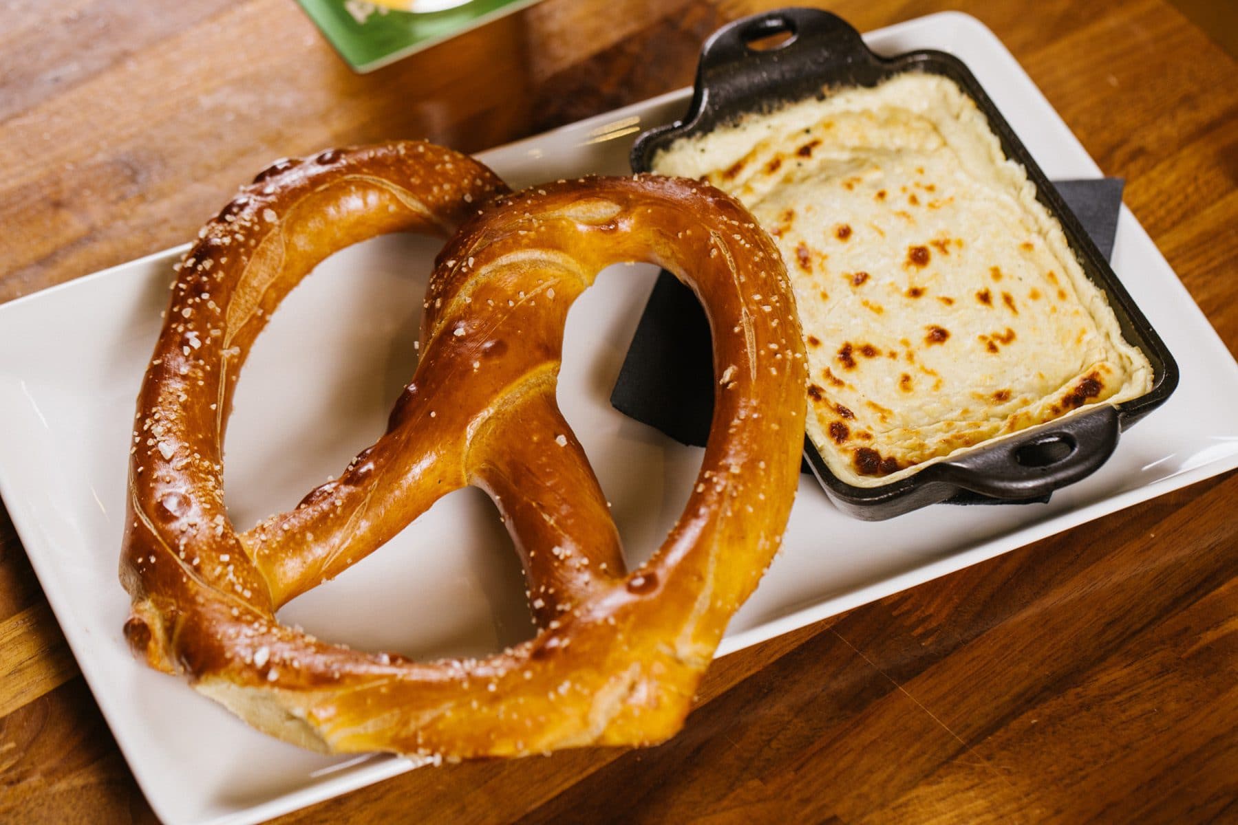 A large pretzel on a plate next to a dish of beer cheese dip