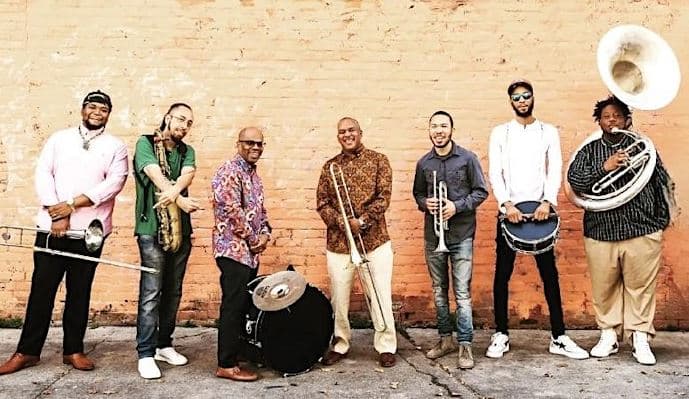 Rebrith Brass Band standing in front of a brick wall holding their instruments