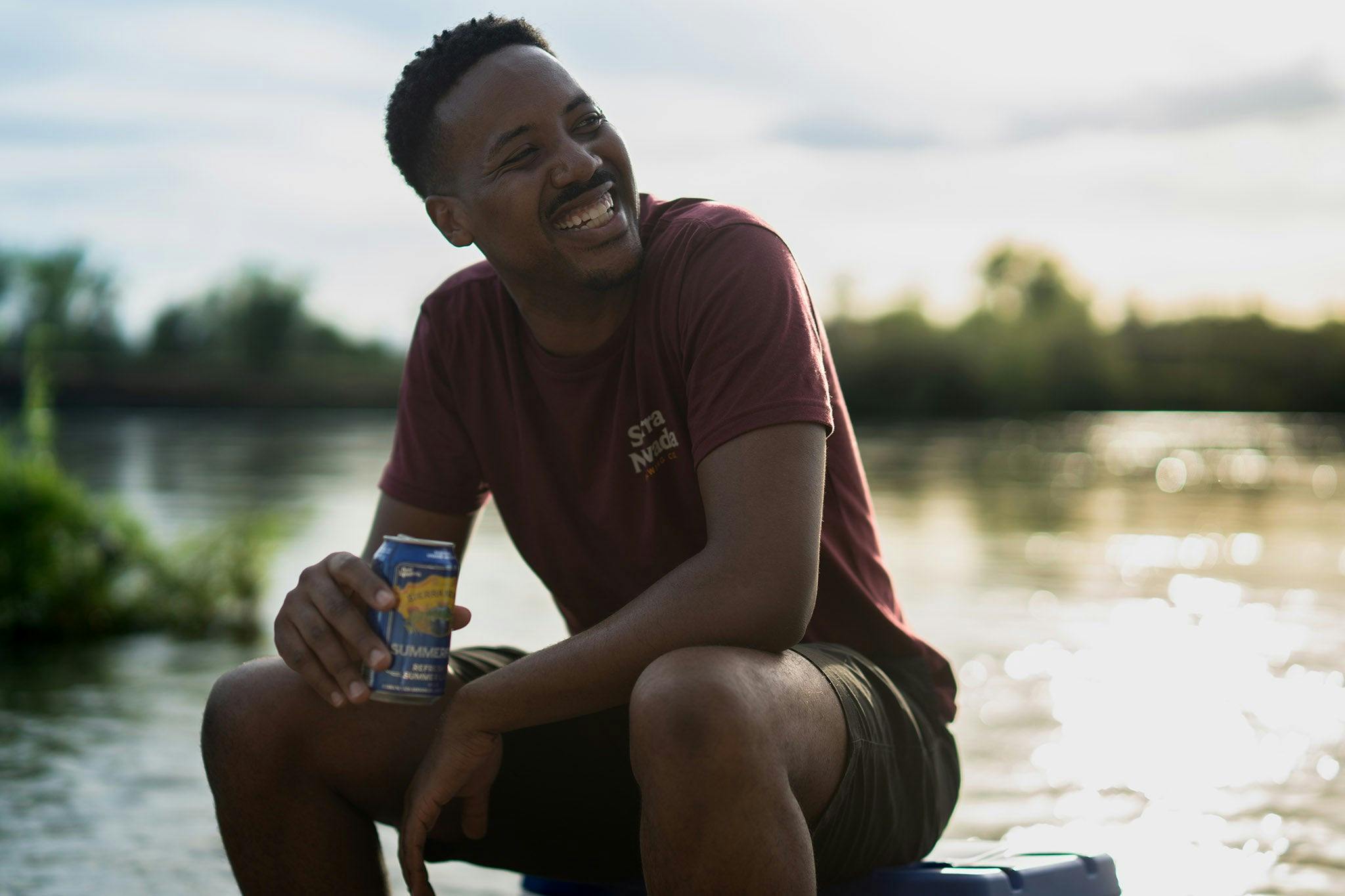 Sierra Nevada Brewing Co. Trail T-Shirt worn by a man sitting on a cooler by a river enjoying a Summerfest beer.