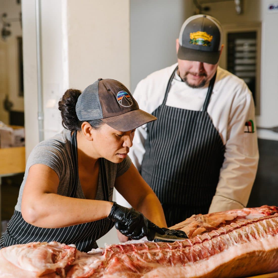 a man watches a women as she cuts a large piece of meat