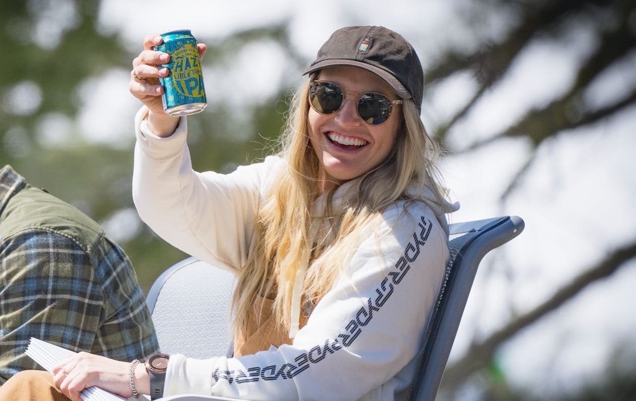 Skier Amie Engerbretson smiling while sitting in a chair outside holding a can of Hazy Little Things IPA beer