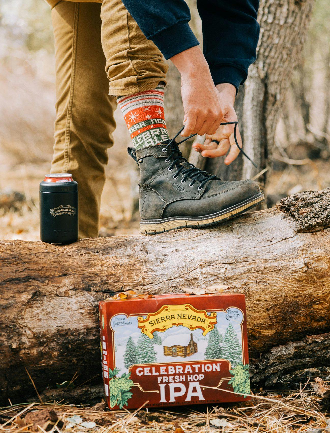 Tying boot on log with pack of Celebration Fresh Hop IPA beers