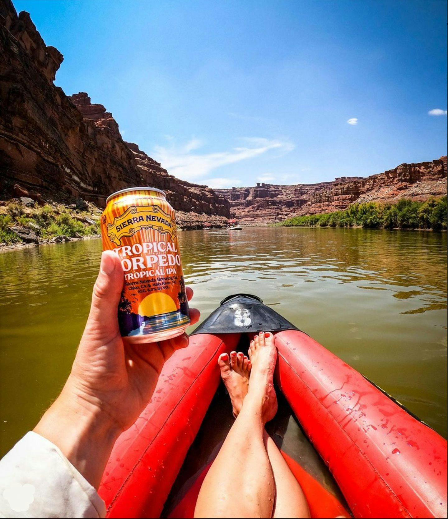 Person holding Tropical Torpedo IPA can on river