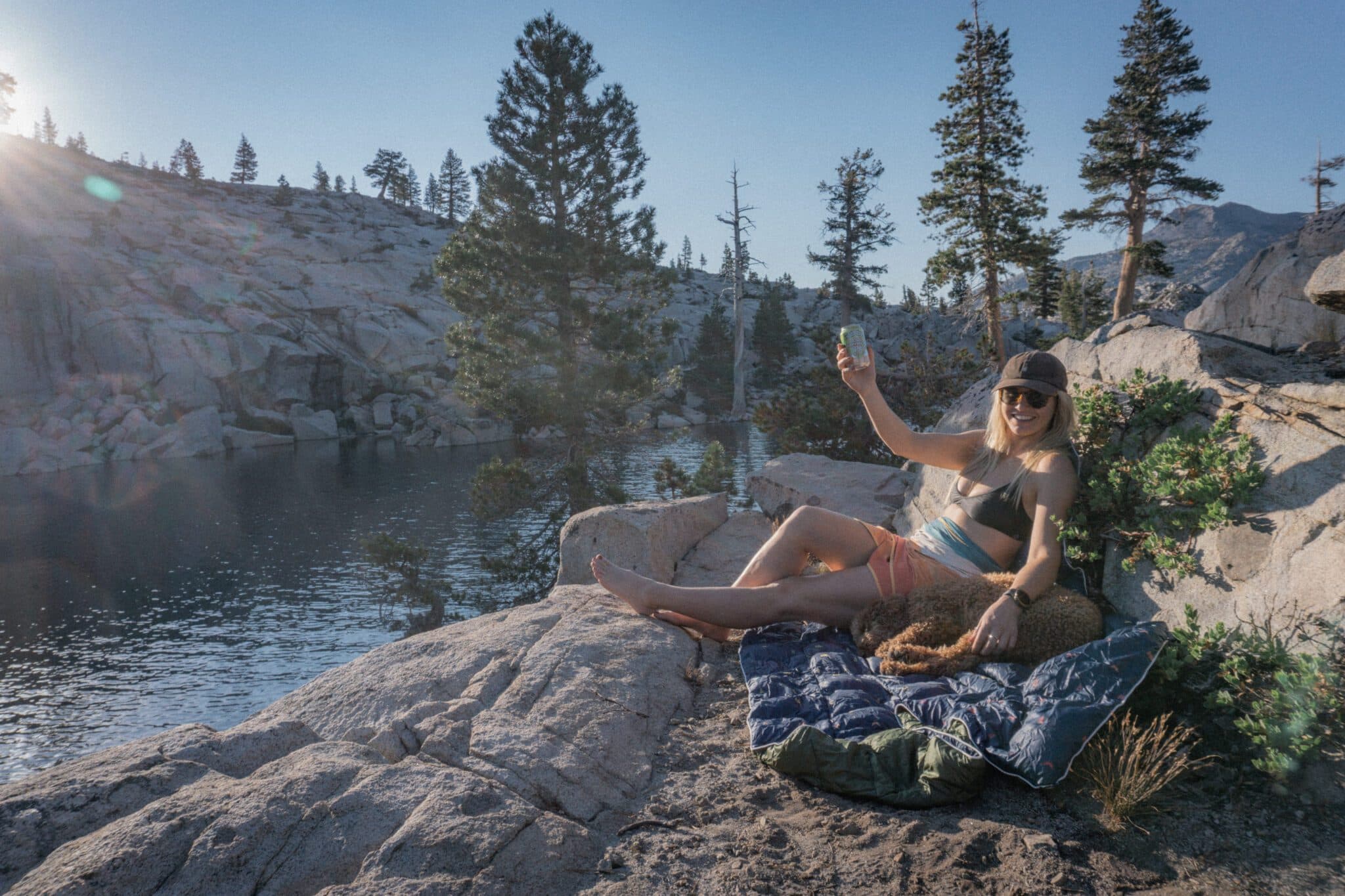 Girl sitting on a trail overlooking water, holding up a beer