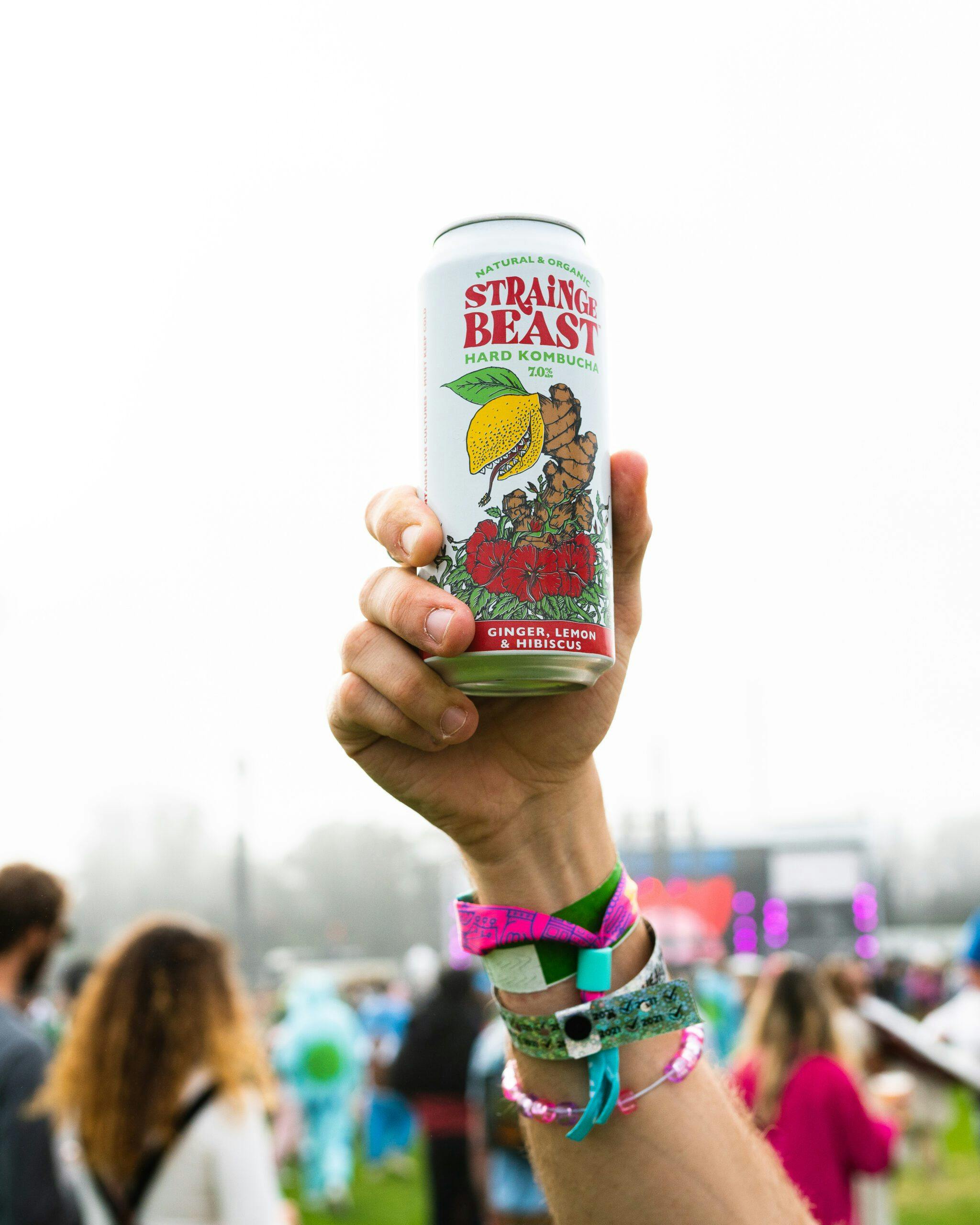 Person in a crowd holding a can of Strainge Beasts Ginger, Lemon & Hibiscus hard kombucha