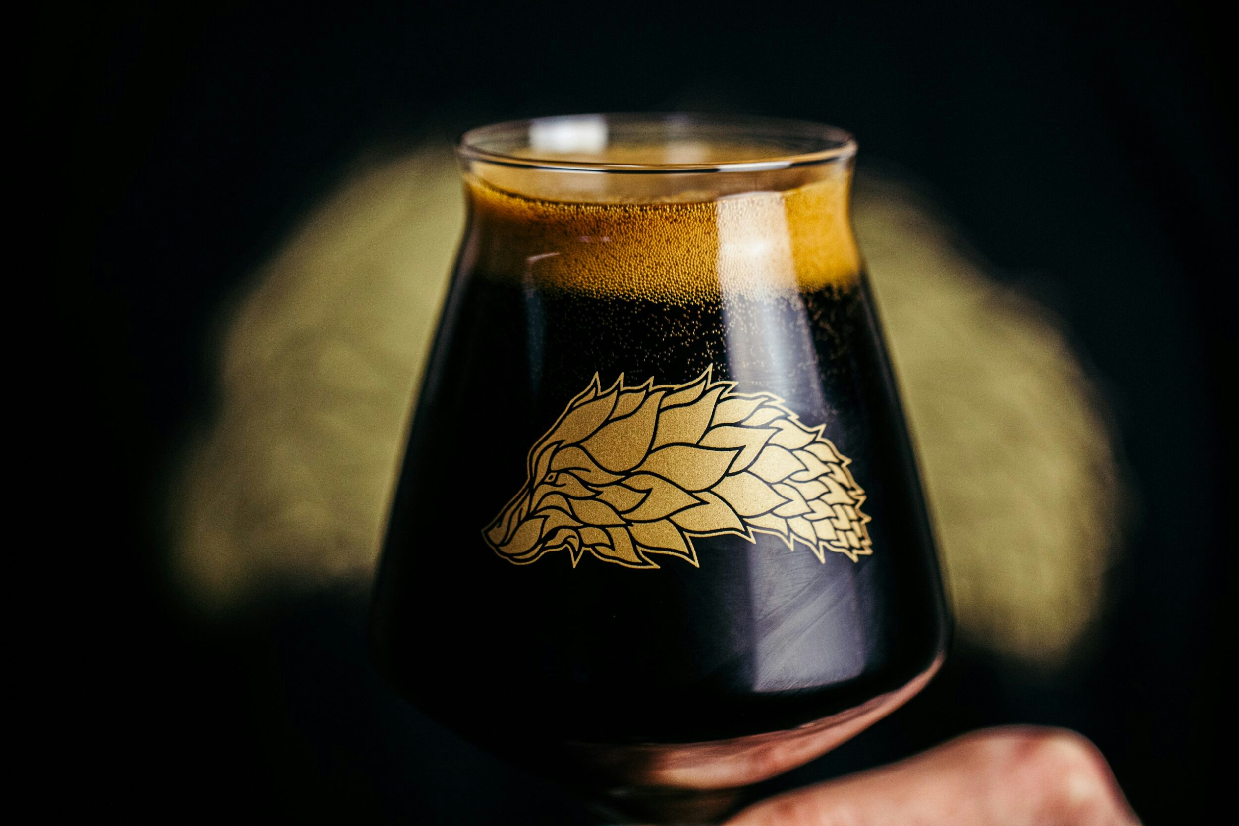 Dark Alpha Hop Society beer in a glass with a hops image