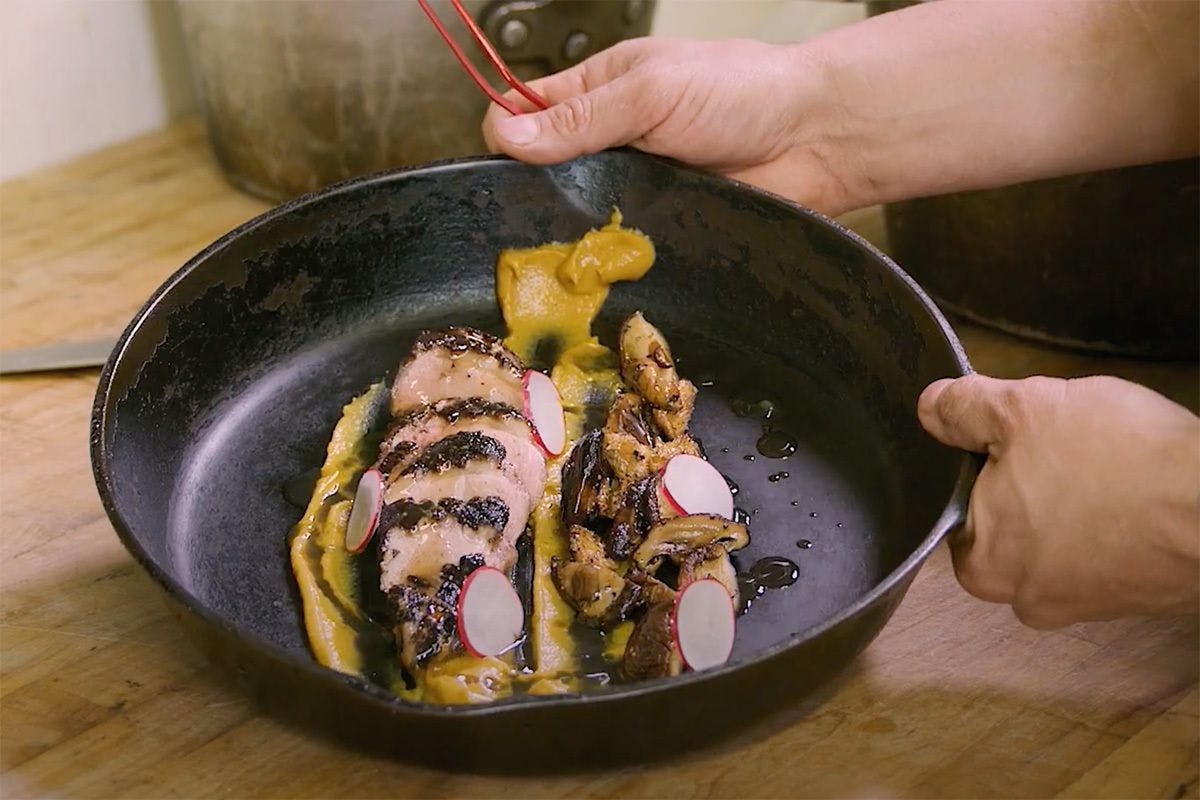 Hands holding a cast-iron skillet filled with a duck confit dish