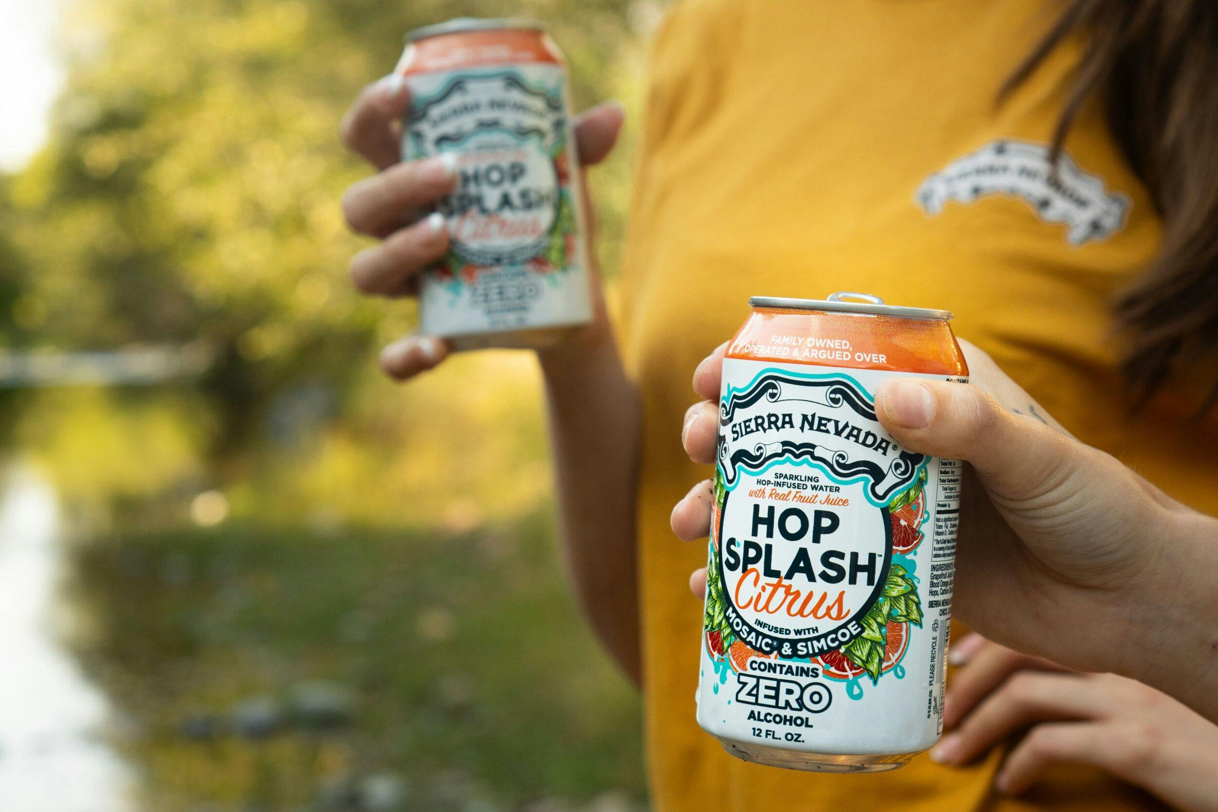 Two people, next to a creek, holding cans of Sierra Nevada Hop Splash Citrus