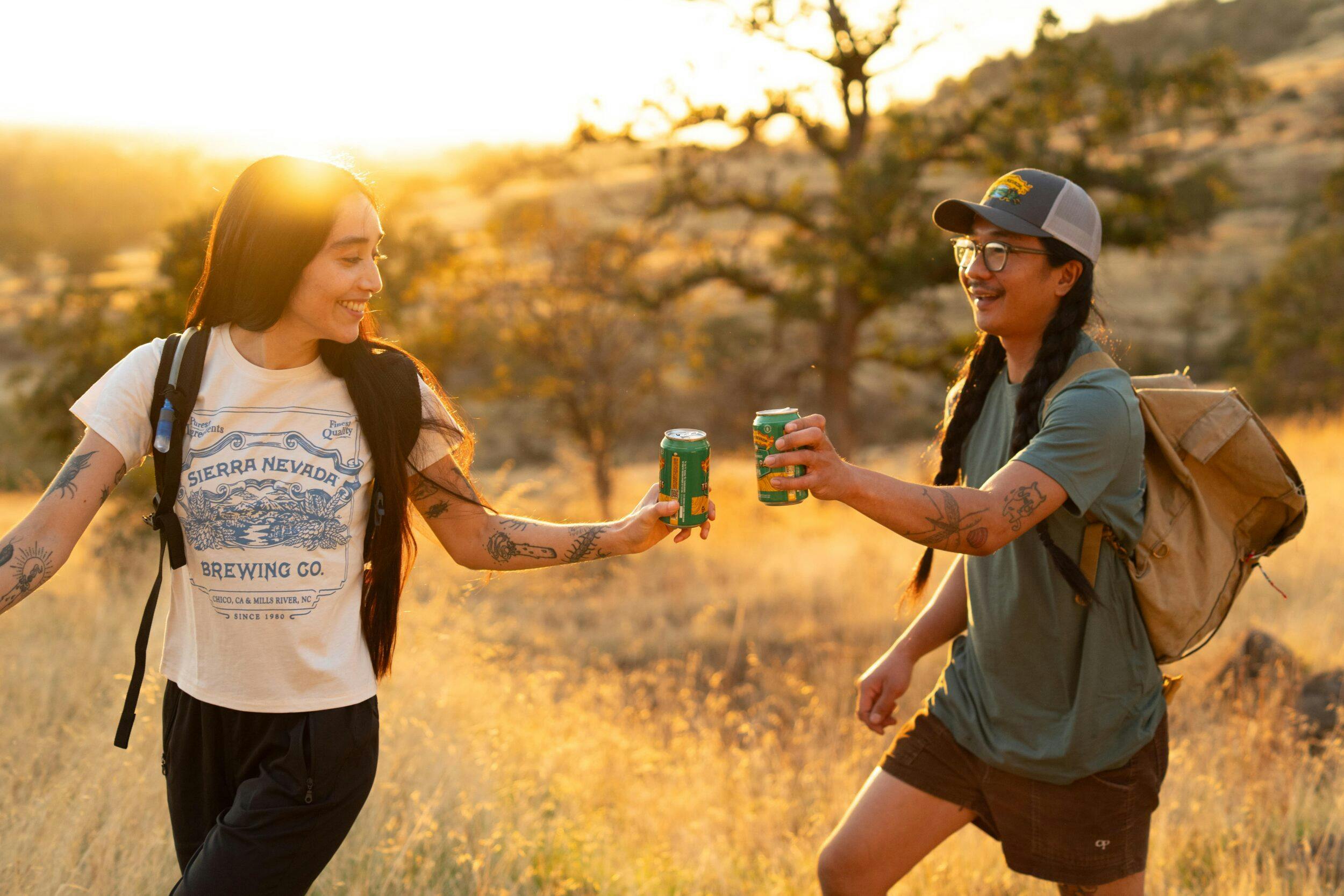 Two hikers on a trail, toasting cans of non-alcoholic Sierra Nevada Trail Pass IPA
